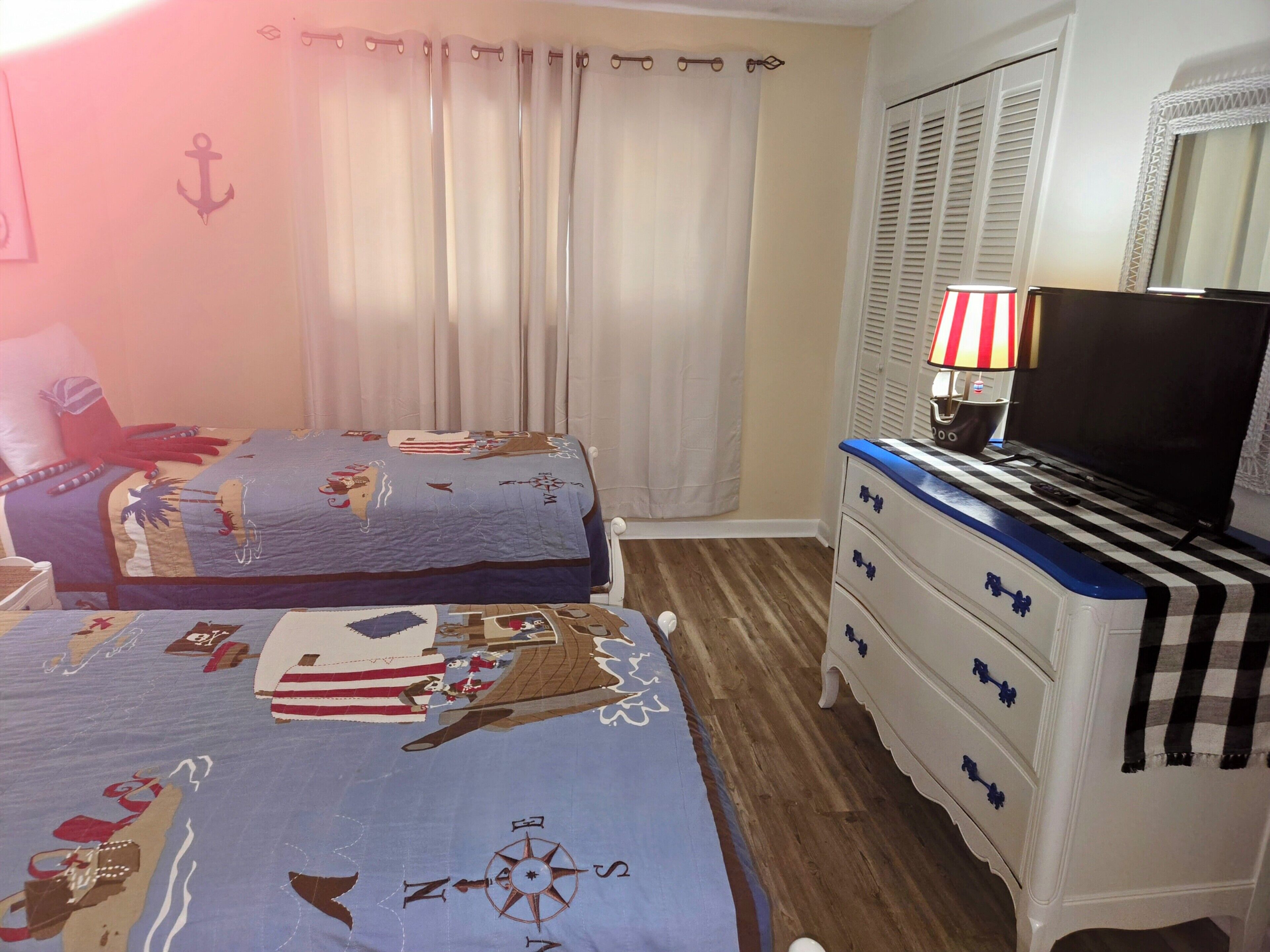 Un dormitorio con dos camas, un aparador, un televisor y una ventana con cortinas.