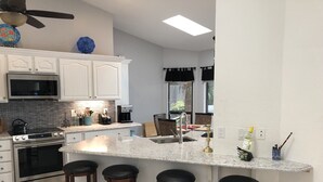 Eine moderne Küche mit weißen Schränken, einer Granit-Arbeitsplatte, einem eingebauten Backofen, einer Mikrowelle und einer Kaffeemaschine. An der Kücheninsel stehen vier Hocker.