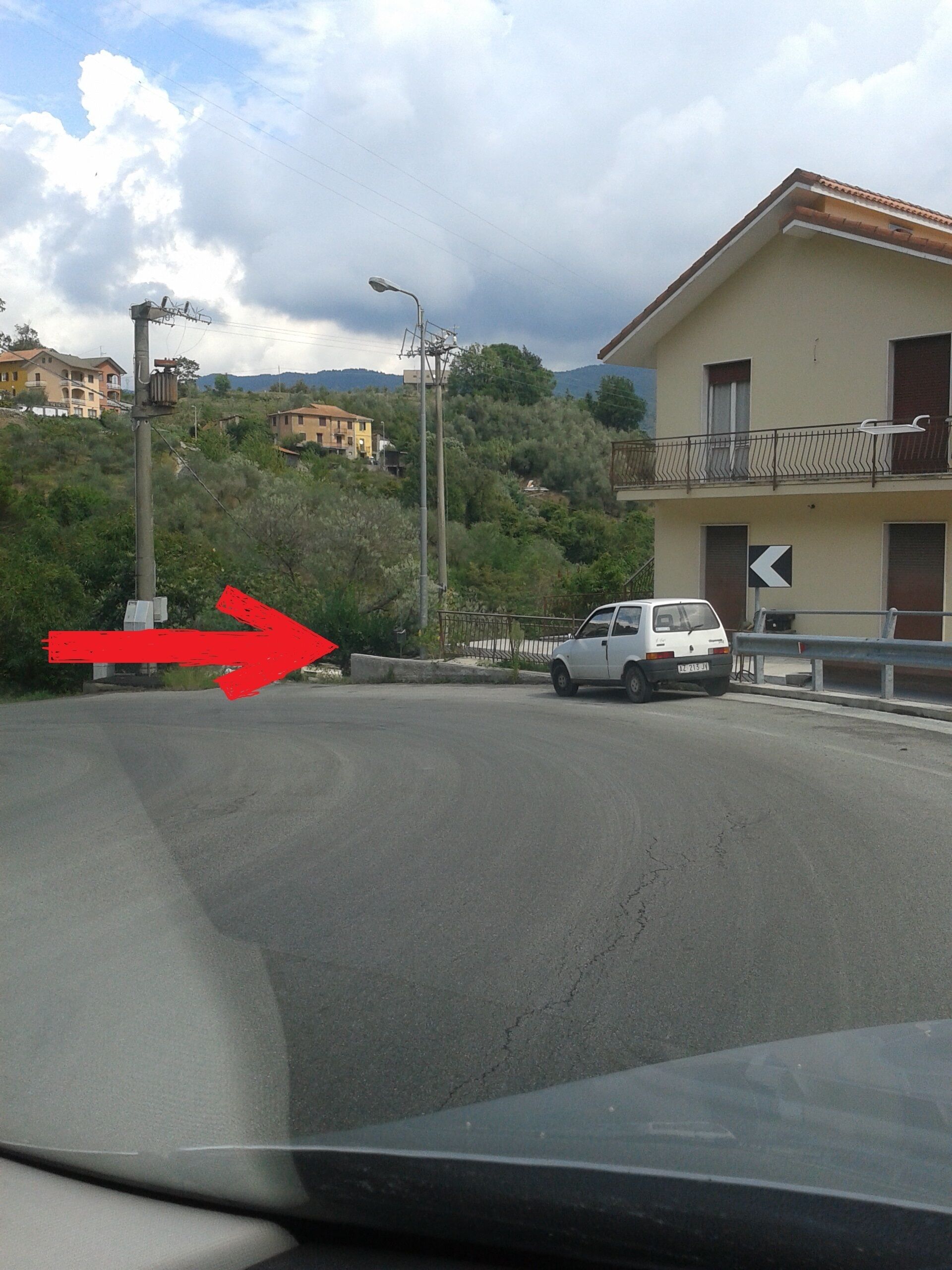 Une route bordée d’un fourgon blanc garé sur le côté, une flèche rouge pointant vers la gauche, et un bâtiment avec un balcon en arrière-plan.