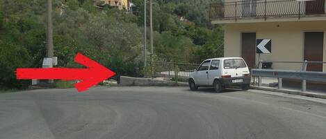 Une route bordée d’un fourgon blanc garé sur le côté, une flèche rouge pointant vers la gauche, et un bâtiment avec un balcon en arrière-plan.