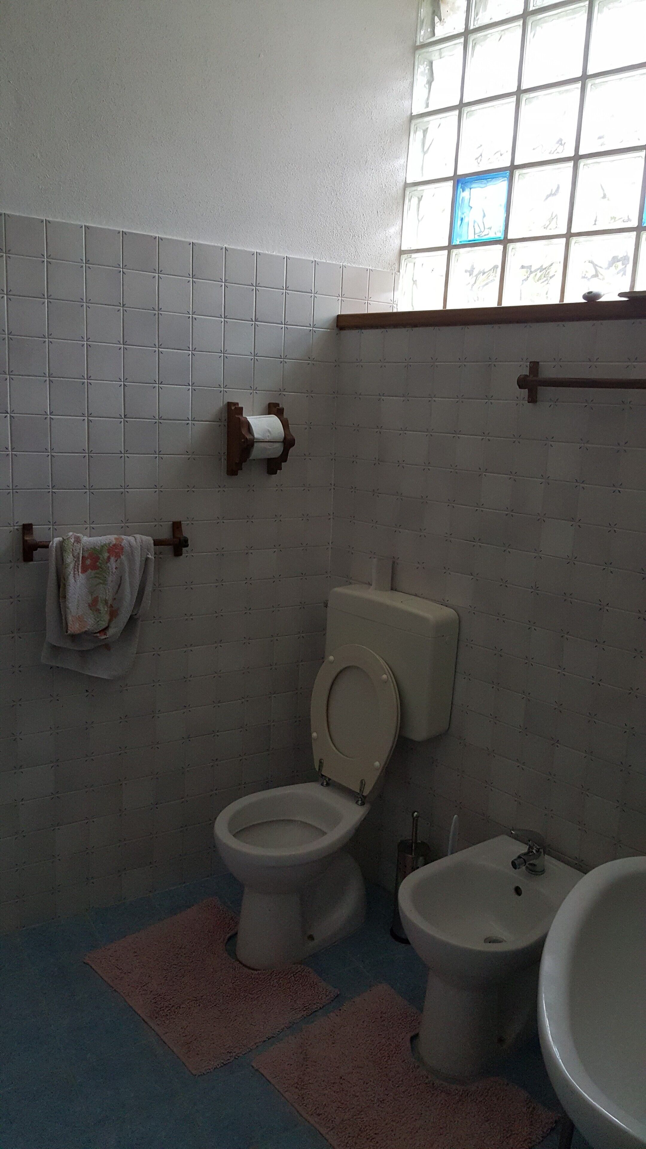 A bathroom with a toilet, bidet, and sink, tiled walls, and a window.