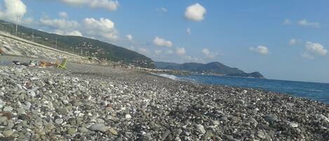 A pebbled beach with a clear sky and distant mountains.