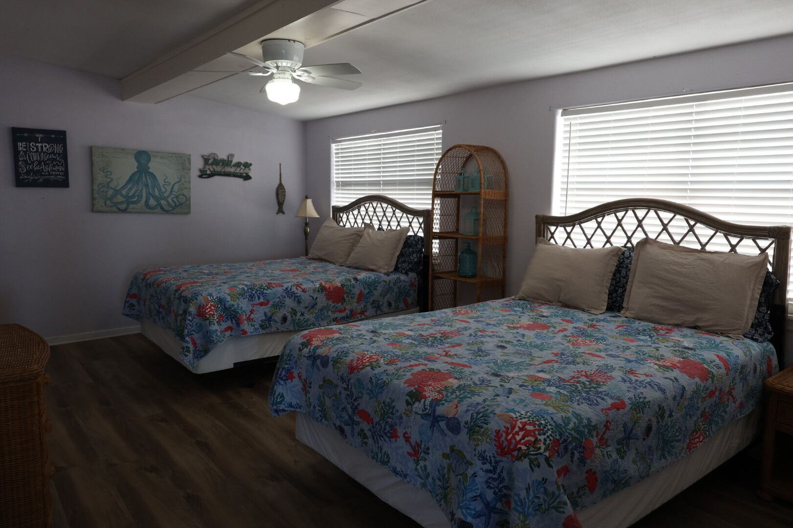 A bedroom with two beds, a ceiling fan, and a window with blinds.