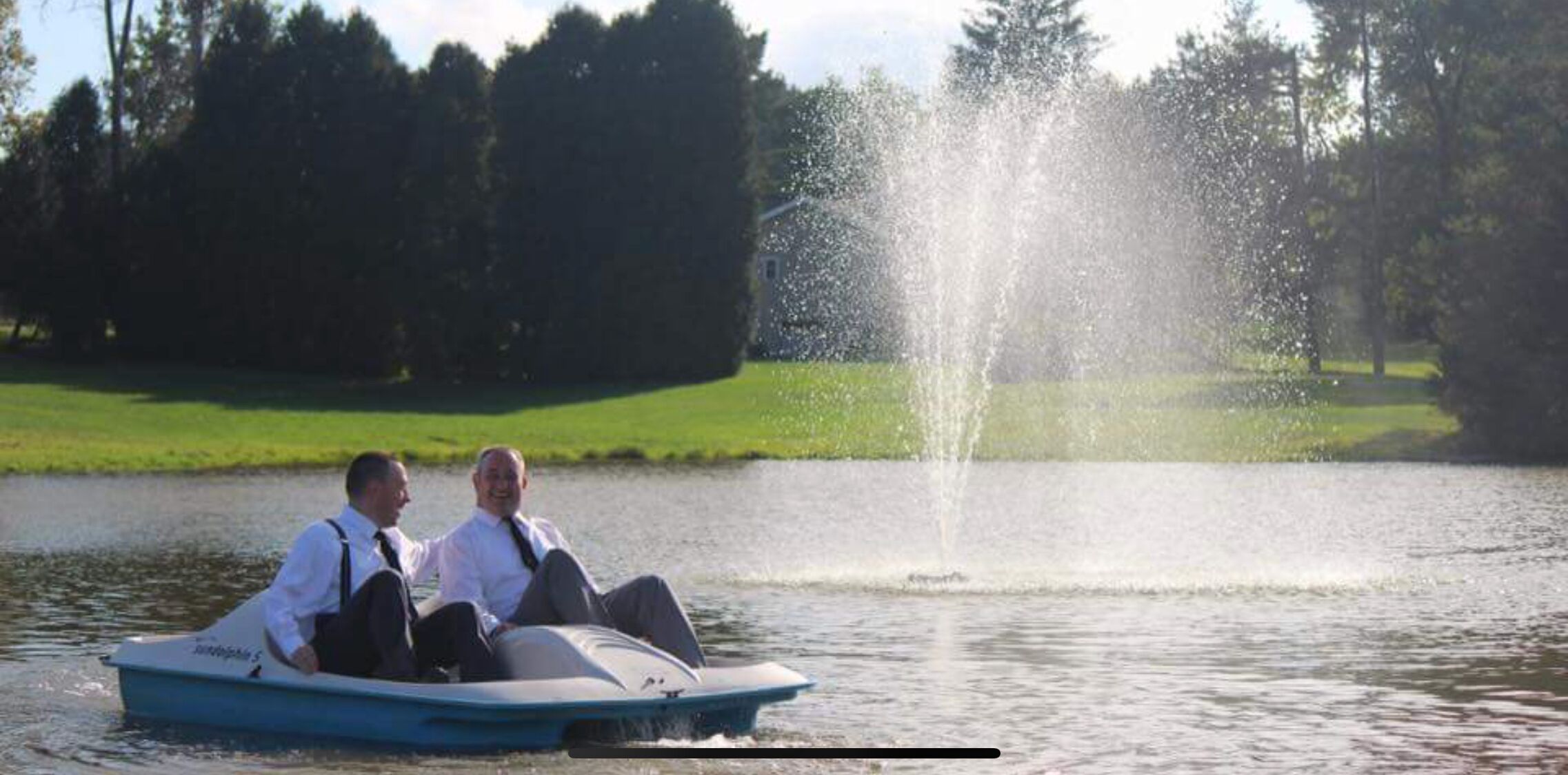 Two people in a boat on a lake with a fountain in the background.