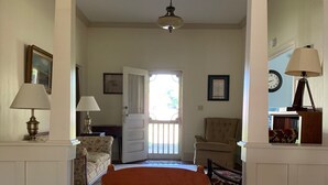 Une chambre à coucher avec un grand lit, un panier en bois rempli de pommes de pin posé sur le lit, un tapis à motifs, une chaise, une lampe et une porte donnant sur une autre pièce.