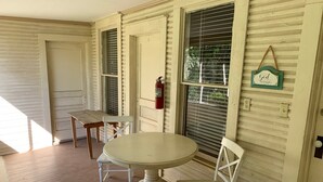 Une pièce avec une table ronde et deux chaises, un extincteur fixé au mur, et un petit panneau suspendu au-dessus d’une fenêtre.