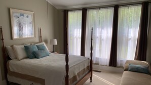 Un lit à baldaquin avec un pied de lit en dentelle, une table de chevet avec une lampe et un tableau floral encadré accroché au mur.