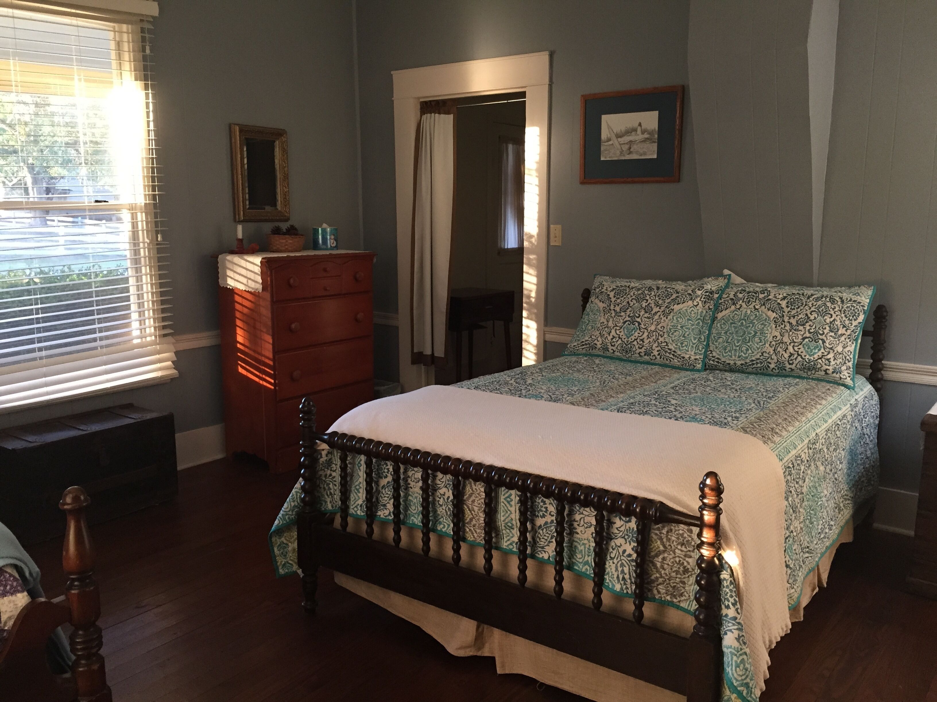 Une chambre à coucher avec un lit en bois, une commode, un miroir et un tableau encadré accroché au mur.