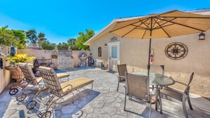 Eine Terrasse mit Steinfliesen, einem Tisch mit Stühlen, einem großen Sonnenschirm und einer Zierwand.