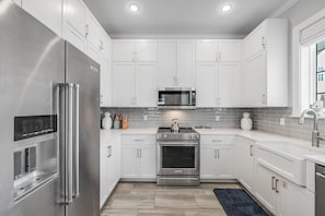 Una cocina moderna con electrodomésticos de acero inoxidable, armarios blancos y salpicadero de azulejos.