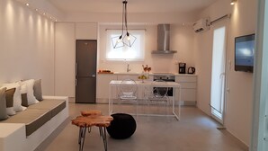 Una cocina moderna con refrigerador empotrado, un comedor con mesa y sillas blancas, y una zona de estar con sofá y reposapiés.