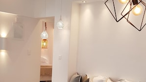 Una cocina moderna con encimera blanca, un bol de vidrio con fruta y una zona de comedor con sillas transparentes.