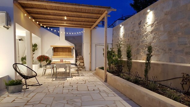 Un patio al aire libre con suelo de piedra, una pérgola de madera y luces colgantes.