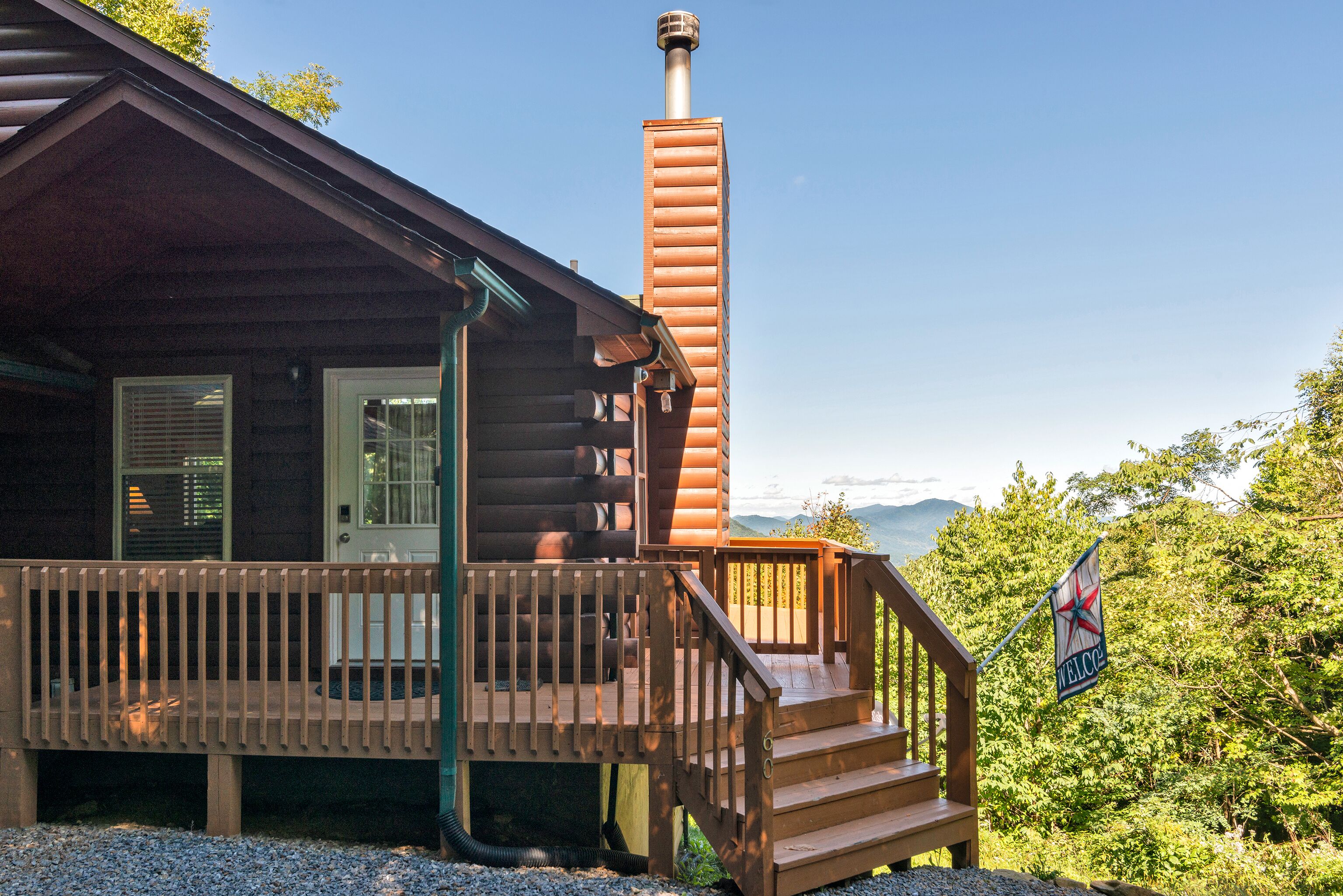 Eine Blockhütte mit Schornstein, einer Holzterrasse und Blick auf die Berge.
