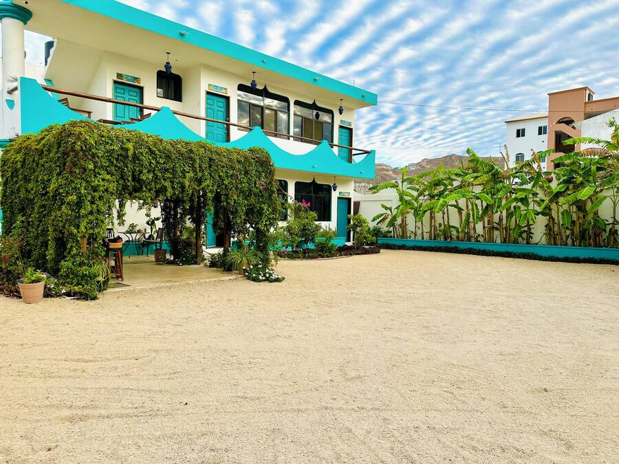 A two-story building with a covered outdoor area, surrounded by greenery and a sandy courtyard.