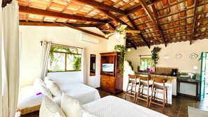 A room with two beds, a wooden ceiling, a TV, a dining area with chairs, and a kitchen area. - CABO BOHEMIA Tropical Garden Studios (Cabo San Lucas)