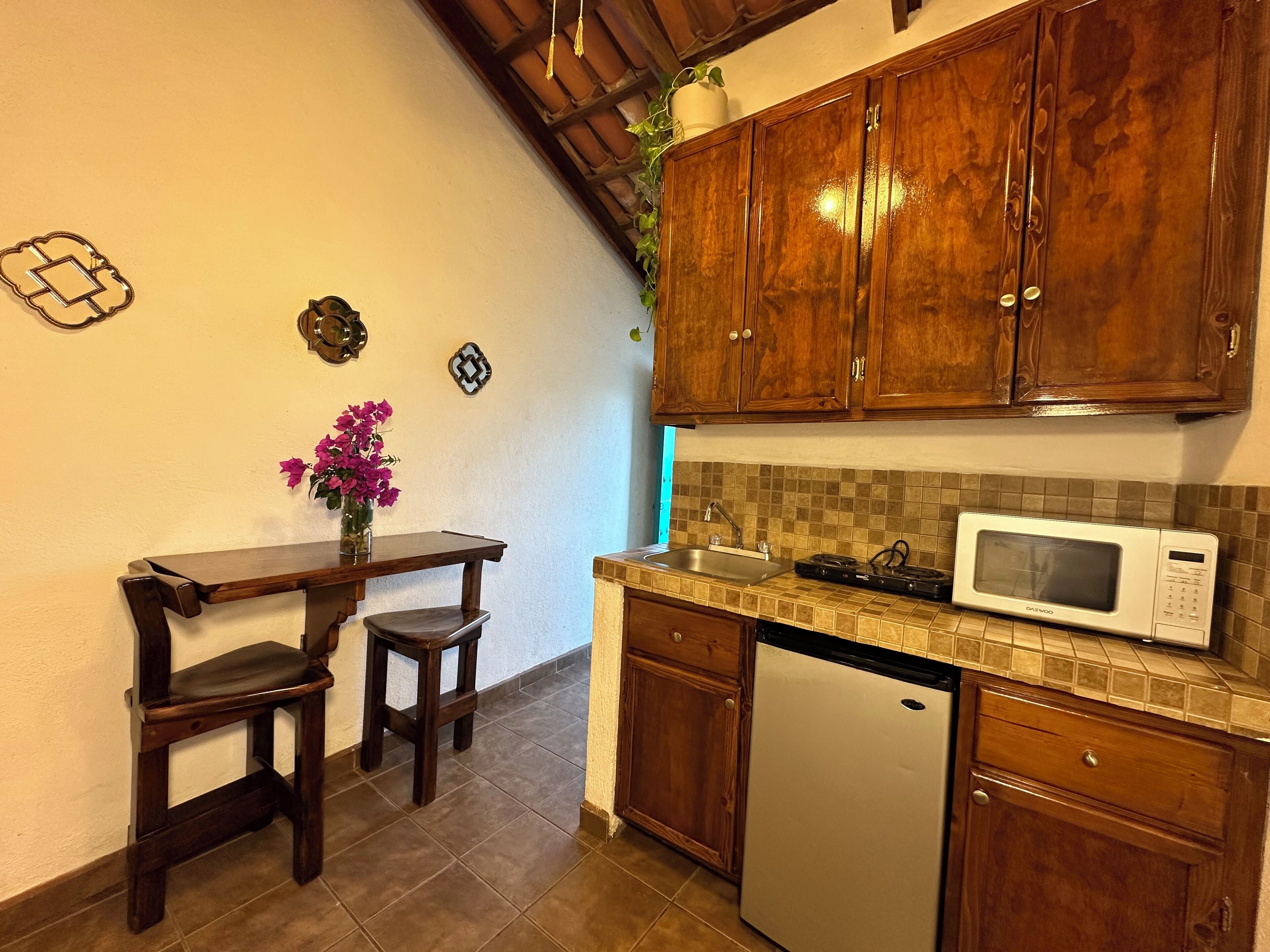 Cocina compacta con armarios de madera, microondas, lavaplatos y una pequeña mesa de comedor con dos taburetes.