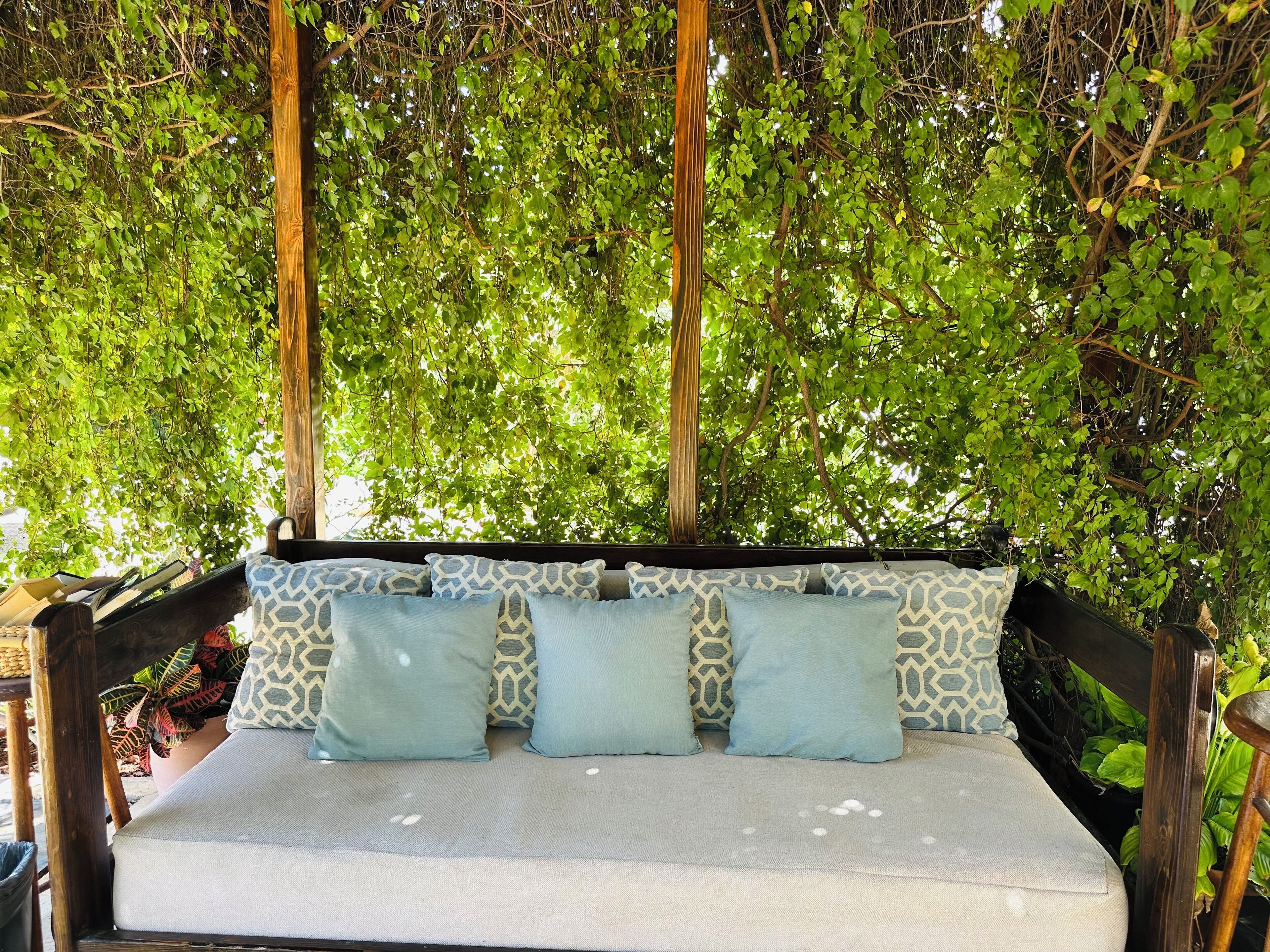 A wooden swing bed with patterned cushions, surrounded by lush green foliage.