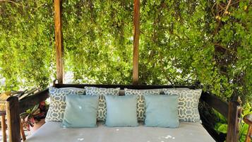 A wooden swing bed with patterned cushions, surrounded by lush green foliage.