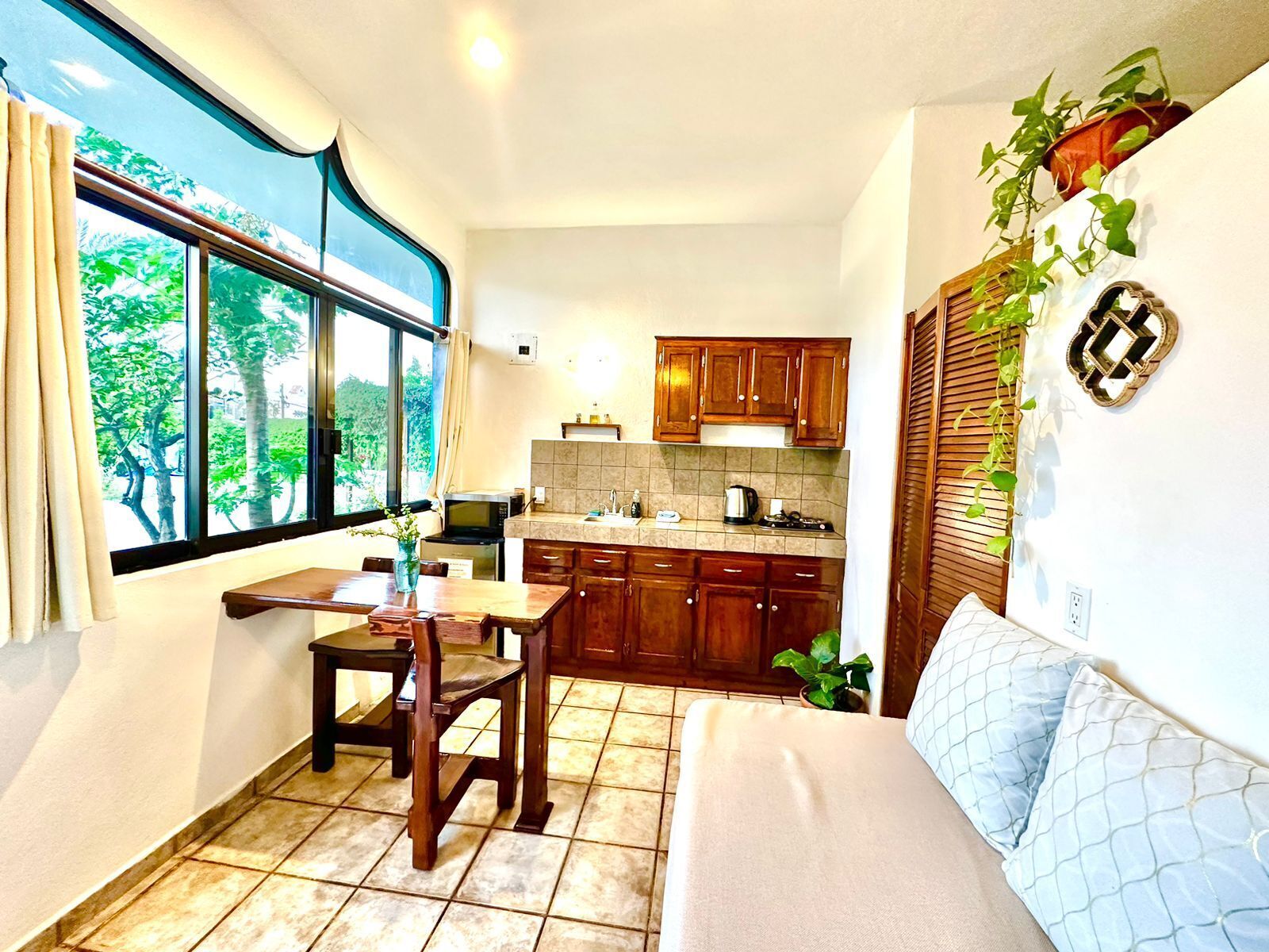 Cocina compacta con armarios de madera, comedor con mesa y sillas, y un ventanal con vistas a la vegetación.