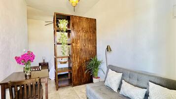 A cozy living room with a wooden bookshelf, a grey sofa, and a dining table with chairs.