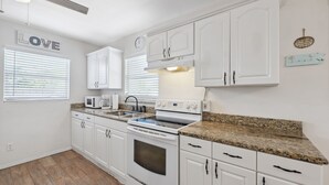 Una cocina con armarios blancos, un microondas, una estufa y un reloj en la pared.