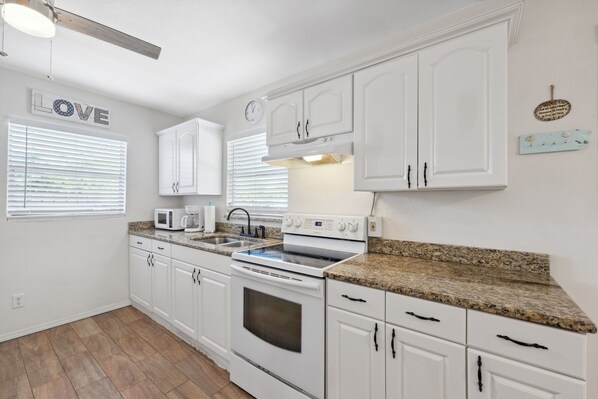 A kitchen with white cabinets, a microwave, a stove, and a clock on the wall.