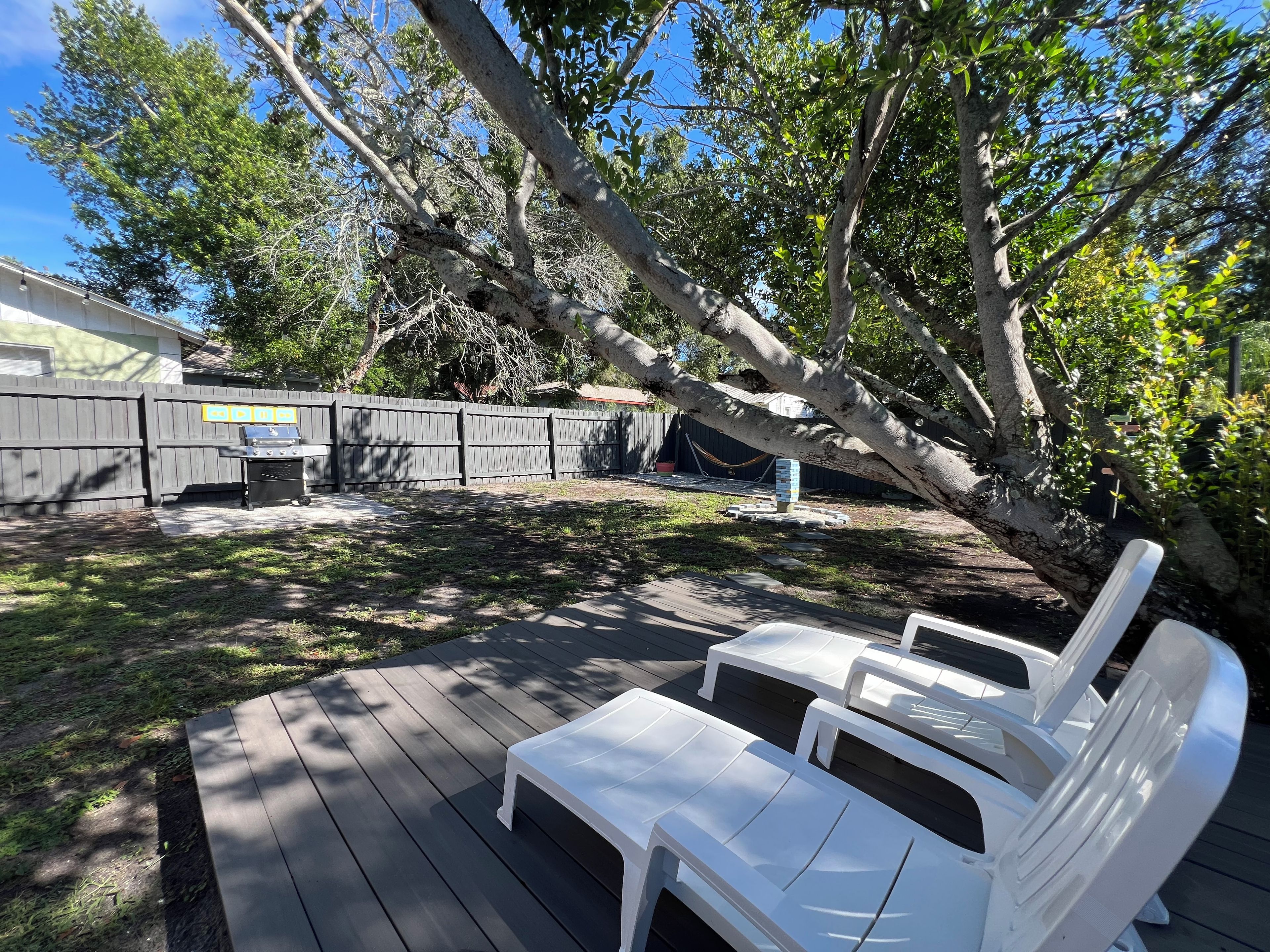 A backyard with a wooden deck, a barbecue grill, and a white plastic chair.