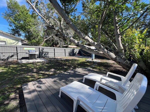 A backyard with a wooden deck, a barbecue grill, and a white plastic chair.