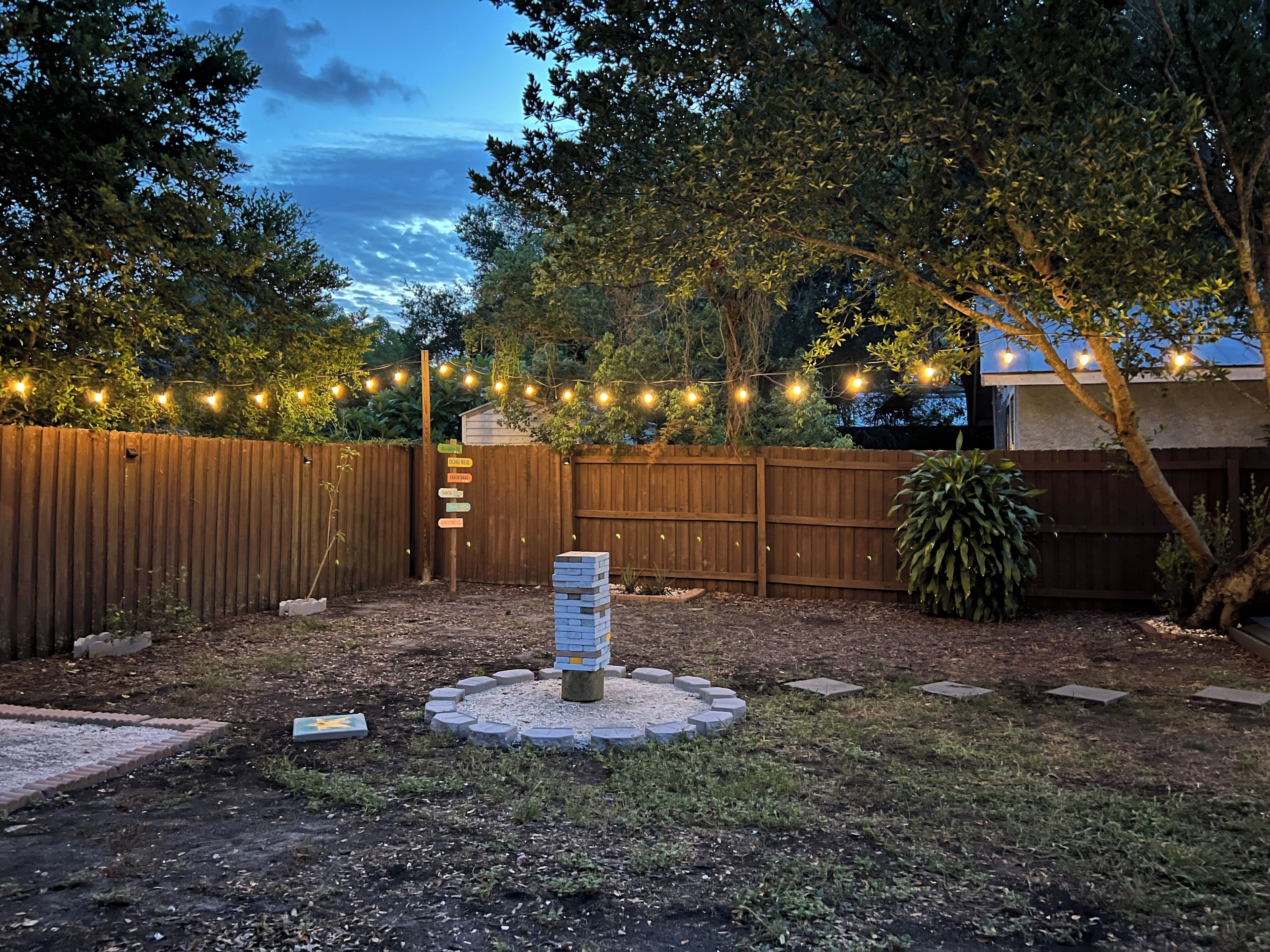 A backyard with a wooden fence, string lights, and a signpost with directions.
