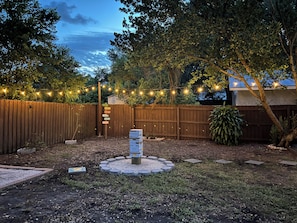 A backyard with a wooden fence, string lights, and a signpost with directions.