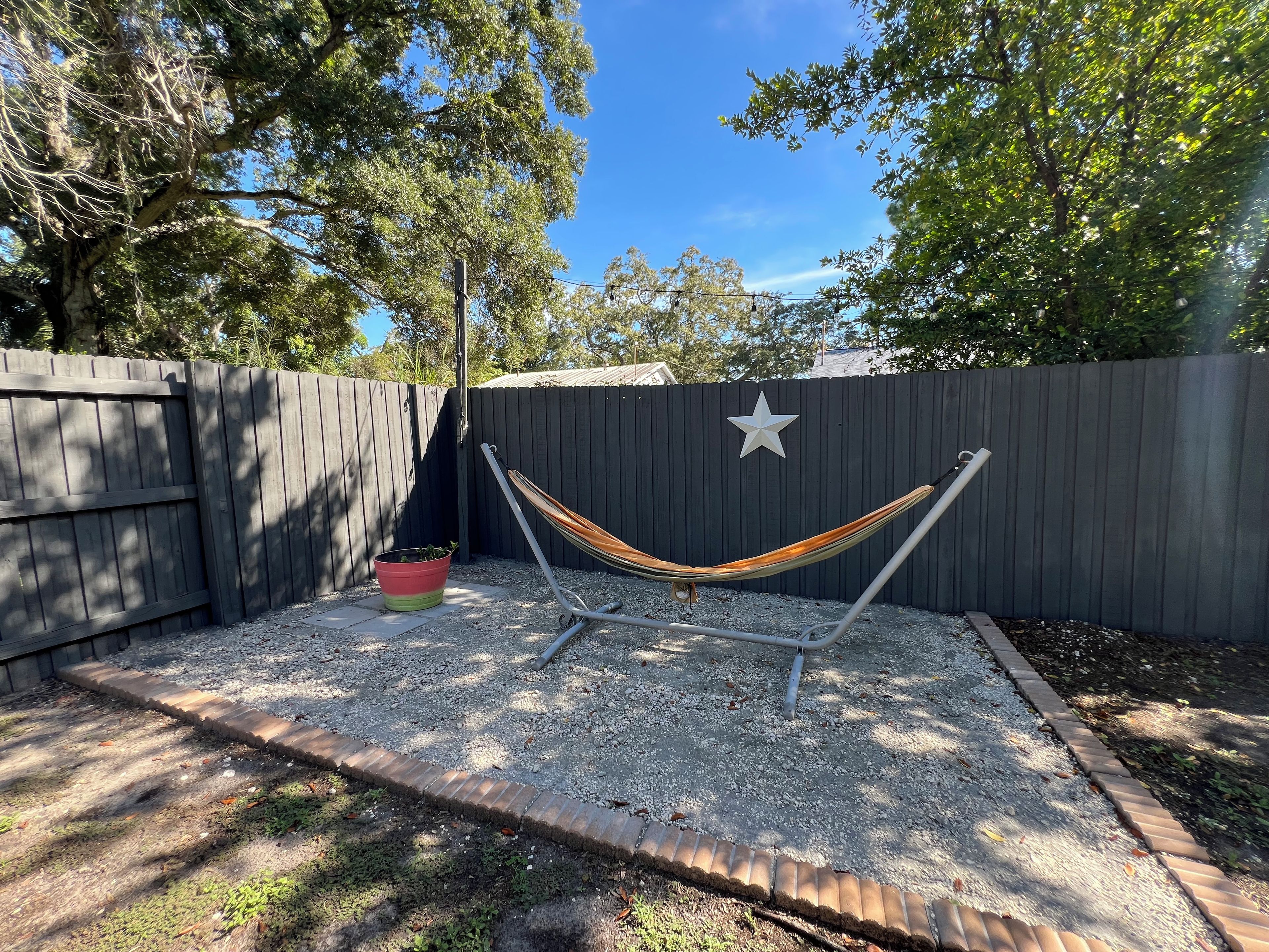 A hammock between two metal poles, a star decoration on a fence, and a potted plant.