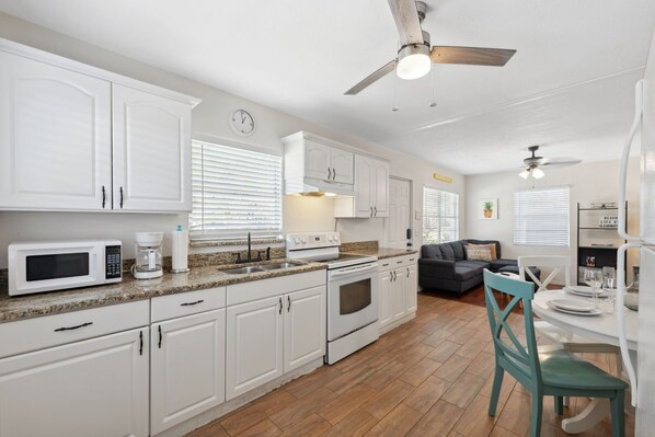A modern kitchen with white cabinets, a microwave, a coffee maker, and a stove. There is a dining area with a table and chairs. - 2BR Home w/ Private Patio, Grill/Near Clearwater Beach (Clearwater)