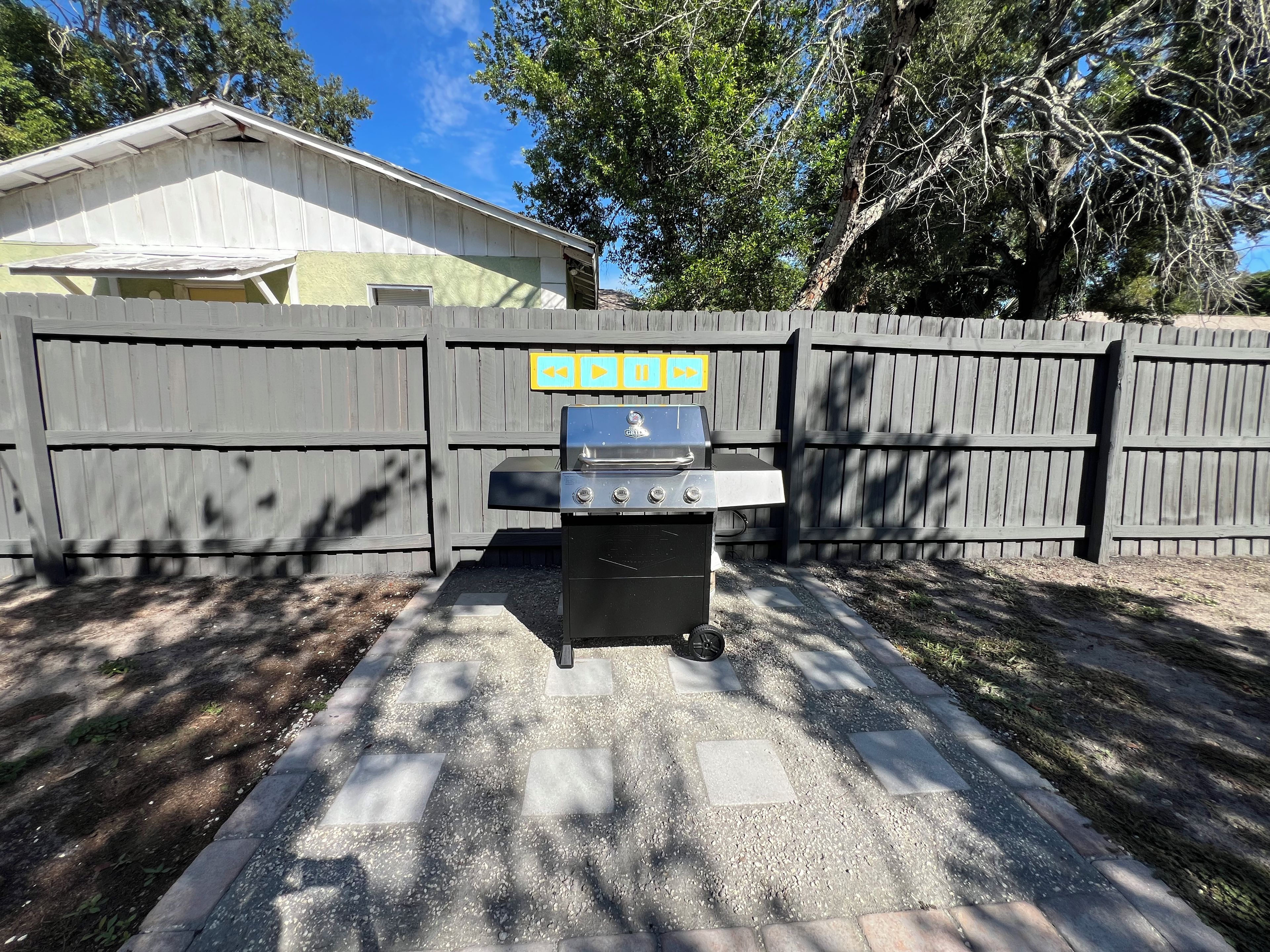 A barbecue grill in front of a wooden fence with a house in the background.