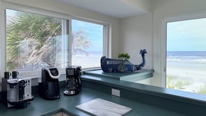 A kitchen with a view of the beach, a coffee maker, and a decorative whale planter.