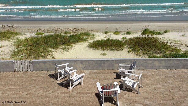 A beach view with white Adirondack chairs and a concrete wall.