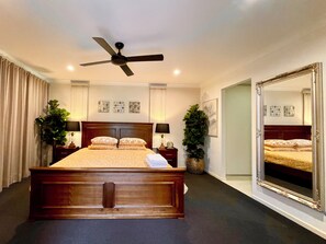 A bedroom with a large bed, a ceiling fan, bedside tables with lamps, a mirror, and wall art. - Spacious Hideaway Retreat, Pool , Spa,  Acreage, Billiards, 7 Bedrooms, Brisbane (Brookfield)