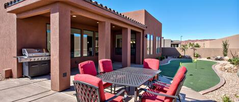 An outdoor patio with a barbecue grill, red chairs, and a table.