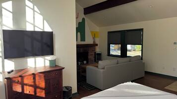 A modern hotel room with a flat-screen TV, wooden dresser, sofa, and a large window offering a view of the outdoors.