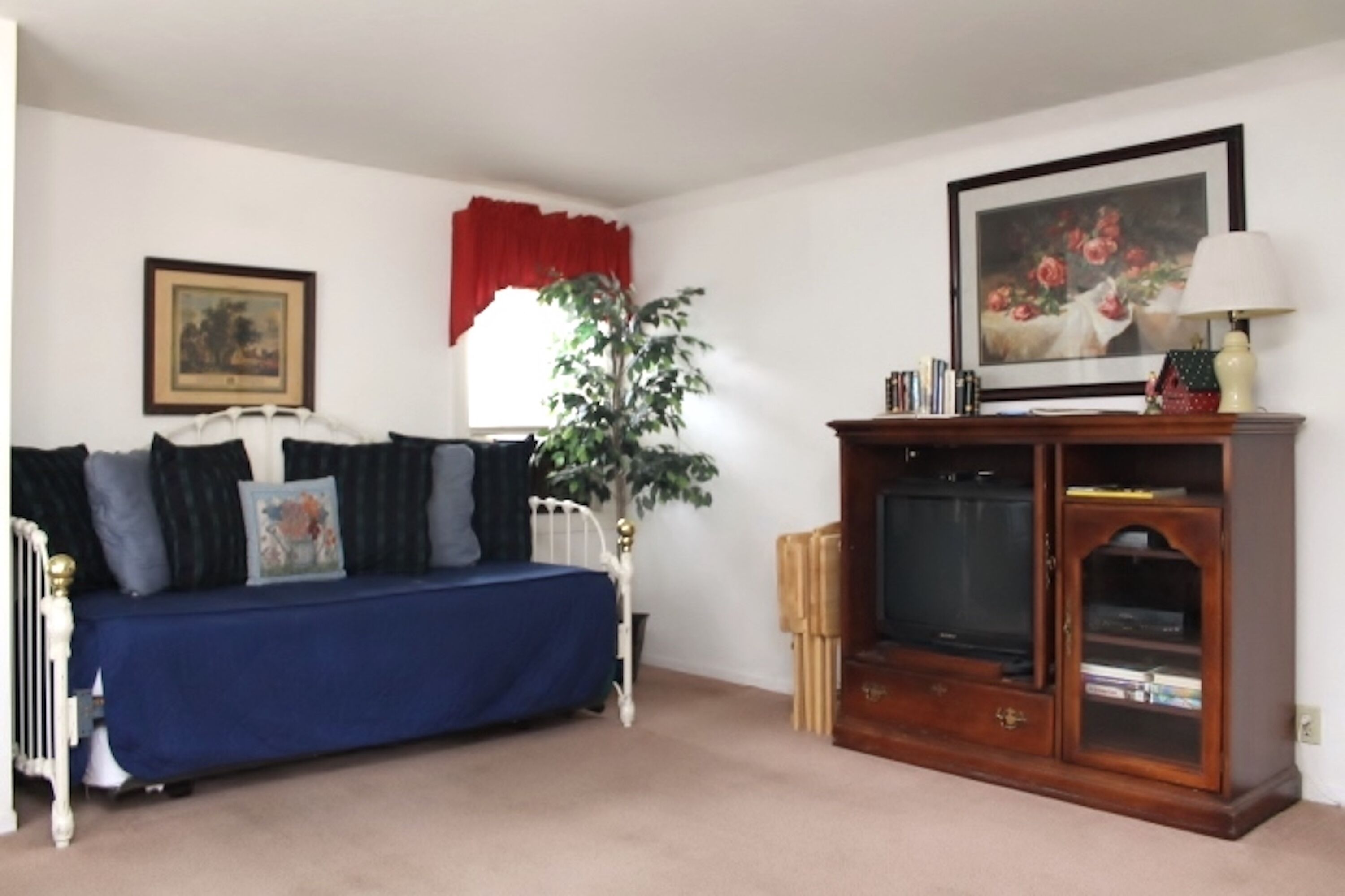 A living room with a blue sofa, a wooden cabinet with a television, a potted plant, and a framed picture on the wall.
