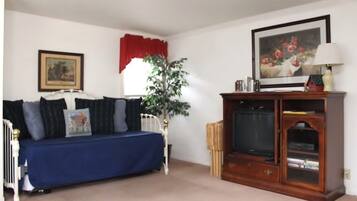 A living room with a blue sofa, a wooden cabinet with a television, a potted plant, and a framed picture on the wall.