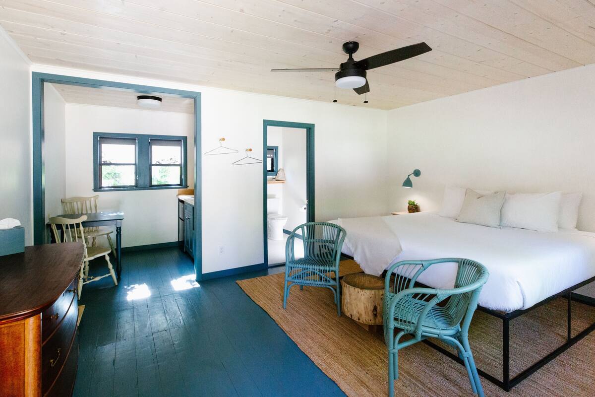A bedroom with a bed, two chairs, a desk, and a ceiling fan.