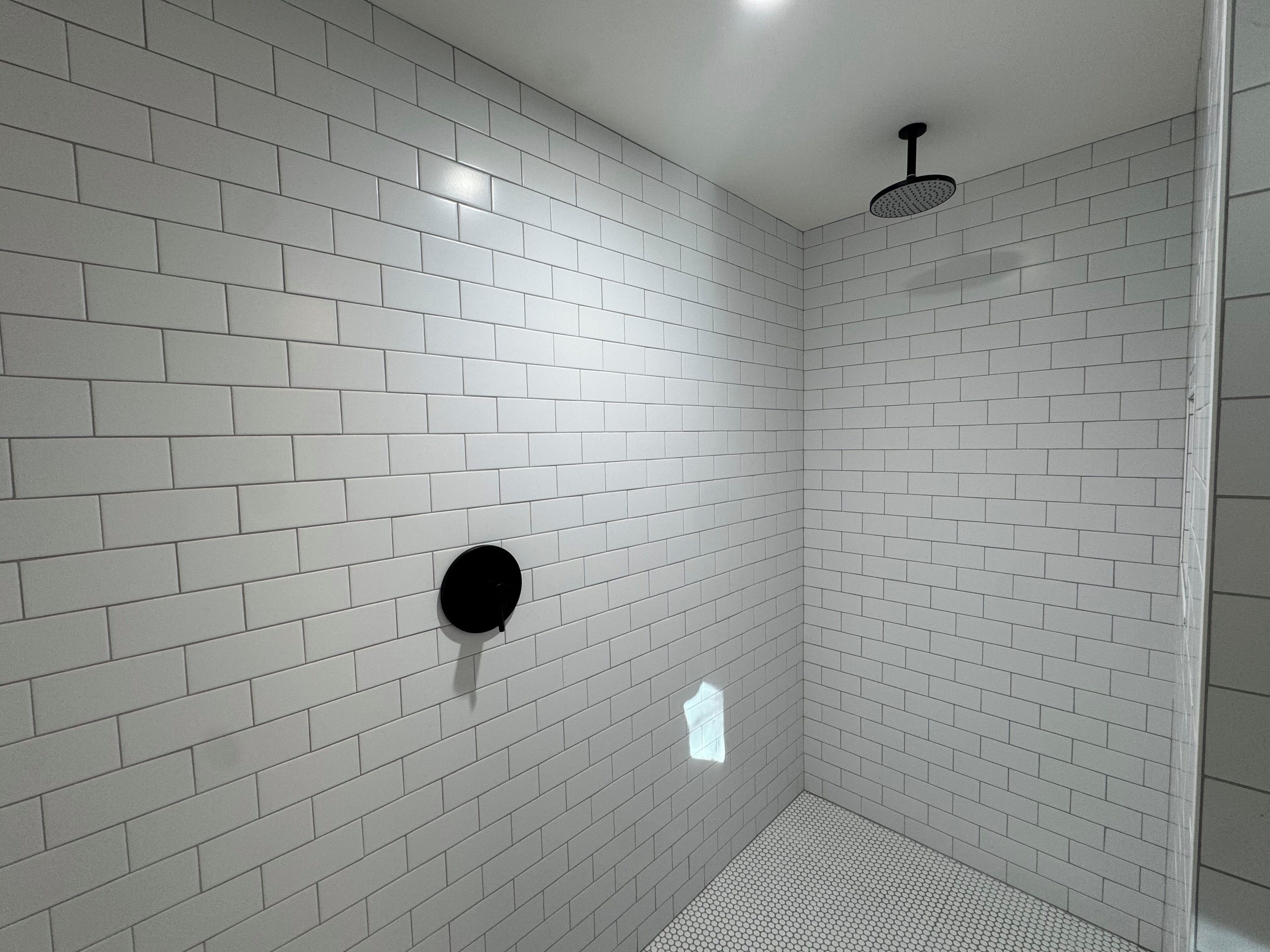 Een moderne douche met witte tegels en een zwart, rond element aan de wand.