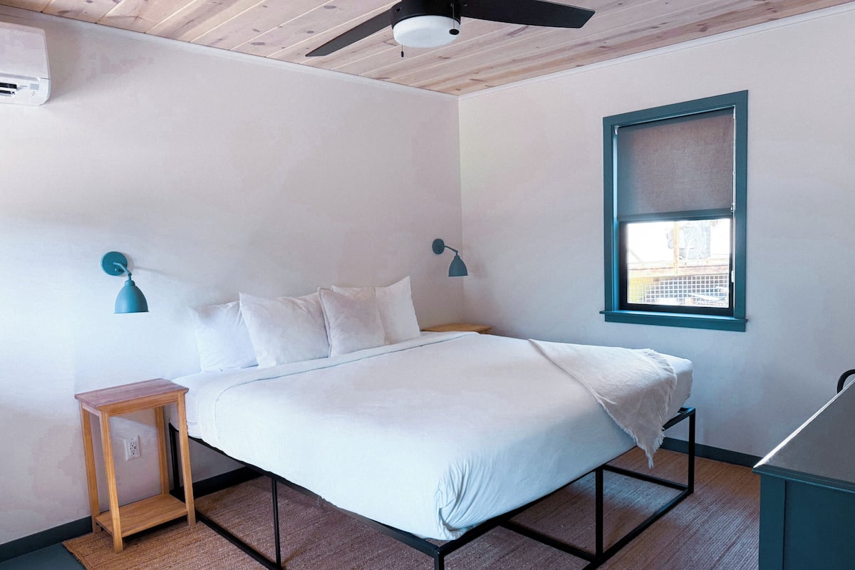A bedroom with a bed, a nightstand, a ceiling fan, a window, and a wall-mounted air conditioner.