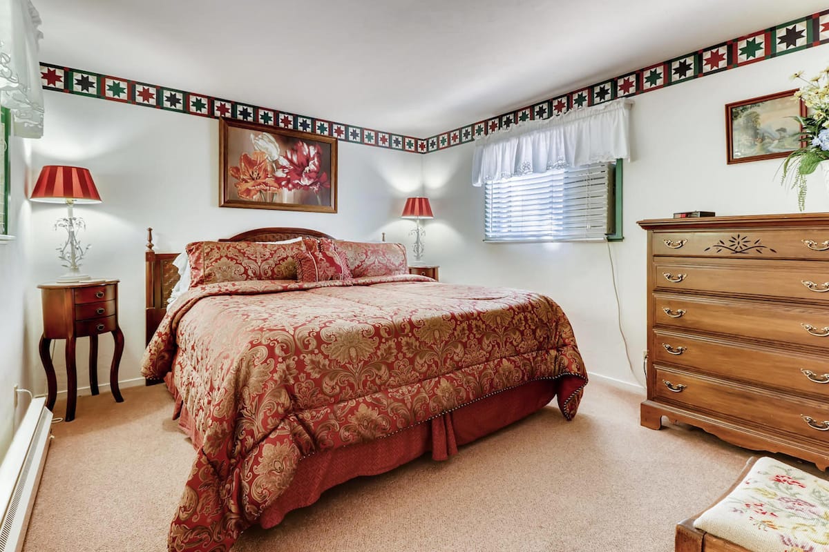 A bedroom with a large bed, a dresser, a nightstand, and a window with blinds.