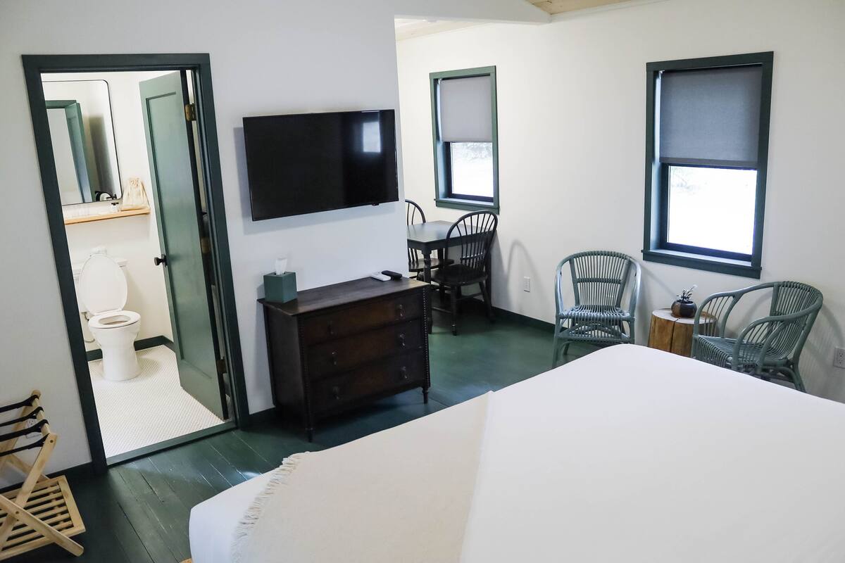 A bedroom with a bed, a dresser, a TV, and a dining area with chairs and a table.