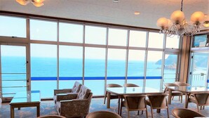 A restaurant with large windows overlooking the sea, featuring a mix of tables and chairs. - Hotel Shiroitodai (Minami)