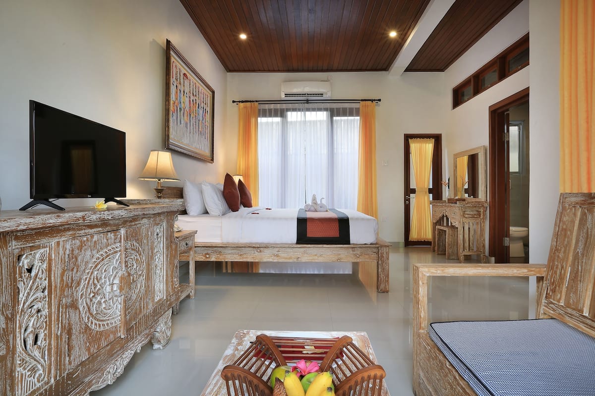 Une chambre d’hôtel avec un lit, une télévision, une commode en bois, une chaise et une table avec des fruits.