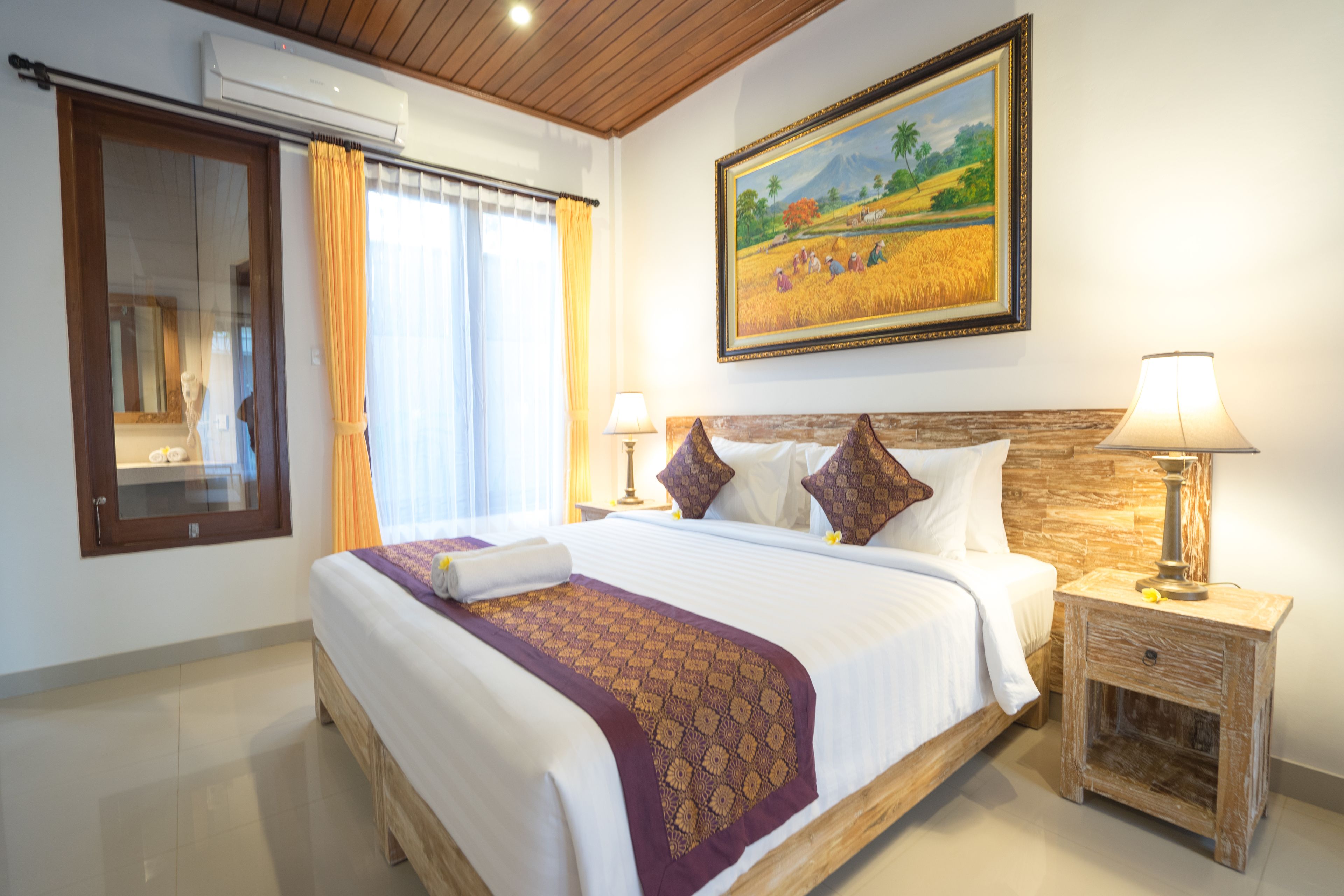 A hotel room with a large bed, two bedside tables with lamps, a painting on the wall, and a window with curtains.