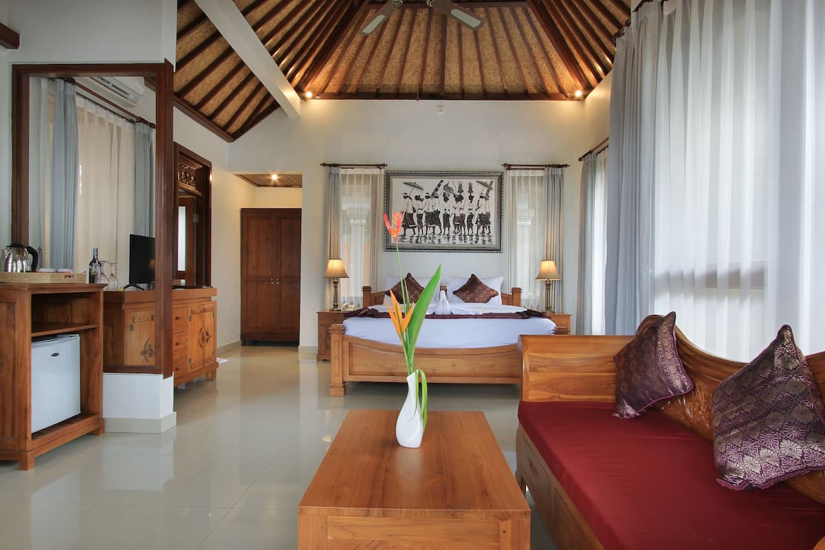 Une chambre d’hôtel avec un plafond en bois, un lit avec un matelas rouge, un bureau en bois orné d’un vase de fleurs et un grand tableau encadré accroché au mur.